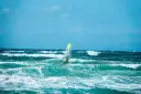 Windsurfer na wzburzonym, turkusowym morzu pod błękitnym niebem.