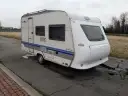 Biała przyczepa kempingowa Hobby 400 de luxe easy z niebieskimi pasami, gotowa na wakacyjne podróże.