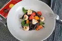 Czarny makaron z krewetkami, pomidorkami i bazylią na talerzu. Obok widoczna paczka spaghetti nero di seppia.