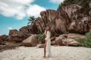 Kobieta w białej narzutce na plaży z granitowymi skałami w tle. Seszele atrakcje to raj dla miłośników przyrody i pięknych krajobrazów.
