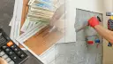 Dłonie z młotkiem i dłutem przy ścianie, obok dokumenty podatkowe i pieniądze.