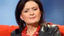 Zofia Czernicka w czarnej skórzanej kurtce i wyrazistej czerwonej biżuterii, siedząca na pomarańczowej kanapie.