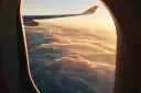 Widok z okna samolotu na chmury o zachodzie słońca, widoczne skrzydło samolotu.