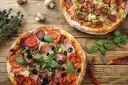 Dwie pizze z dodatkami: salami, pomidory, oliwki, szynka, pieczarki i bazylia.