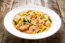 Makaron spaghetti z łososiem i szpinakiem na białym talerzu, na drewnianym tle.