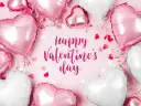Mnóstwo różowych i białych balonów w kształcie serc, ozdobionych wstążkami i konfetti, tworzy romantyczną atmosferę. Napis "Happy Valentine's Day" dopełnia całość.