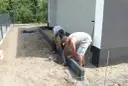 Dwóch mężczyzn układa suchy beton pod obrzeża wokół domu.