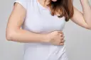 Kobieta w białej koszulce trzyma się za bok, odczuwając ból po lewej stronie brzucha.