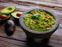 Guacamole w kamiennym moździerzu z awokado i kolendrą na drewnianym tle.