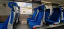 Wygodne, niebieskie fotele w wagonach PKP Intercity bez przedziałów. Widok na mijany krajobraz i inne wagony.