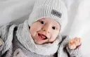 Uśmiechnięte niemowlę w szarej czapce i szaliku.