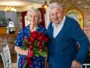 Para świętuje 70 rocznicę ślubu. Ona trzyma bukiet czerwonych róż, on stoi obok.