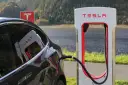 Czarny Tesla podłączony do ładowarki Supercharger nad jeziorem.