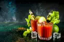 Dwa drinki Krwawa Mary z łodygami selera, limonką i piklami, ozdobione przyprawami i lodem.