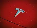 Błyszczące logo Tesli na czerwonej karoserii z kroplami deszczu. Czy Tesla jest tylko elektryczna?