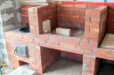 Budowa solidnego grill z cegły klinkierowej. Widać palenisko i drzwiczki.