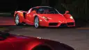 Czerwone Ferrari Enzo zaparkowane nocą na drodze, z innym czerwonym samochodem w tle.