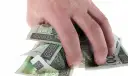 Dłoń trzyma plik polskich banknotów 100 zł. Może to symbolizować zwrot refinansowania lub po prostu oszczędności.