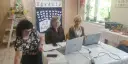 Trzy kobiety pracują przy stołach w sali, która wygląda jak szkoła specjalna. Na ścianie wisi tablica z motylami i napisem "Zgadula".