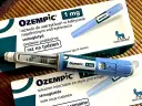 Dwa opakowania i dwa peny leku Ozempic 1 mg na podkładce bambusowej.