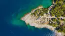 Widok z lotu ptaka na malowniczy camping Makarska. Kamieniste wybrzeże, turkusowa woda i mnóstwo przyczep kempingowych wśród drzew.