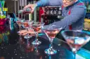 Barman nalewa różowy drink do kieliszków koktajlowych na czarnym blacie.