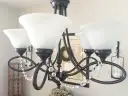 Ciemny metalowy żyrandol z białymi kloszami i kryształkami.