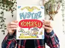 Okładka książki "Mistrz Komiksu" z rysunkami postaci i słońca, trzymana przez ręce.