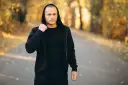 Mężczyzna w czarnej bluzie męskiej Guess z kapturem, stojący na ścieżce w jesiennym parku.
