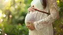 Brzuch kobiety w ciąży, otulony koronkową sukienką. Delikatne światło i zieleń natury tworzą ciepłą atmosferę, jakby wspierały jej luteina dopochwowa w ciąży.