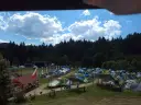 Pole namiotowe na festiwalu w Solinie. Tysiące namiotów pod błękitnym niebem z chmurami, w tle las i scena festiwalowa.