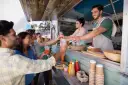 Uśmiechnięci ludzie odbierają napoje od barmanów z food trucka.