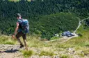 Turysta z plecakiem schodzi po kamienistej ścieżce w Karkonoszach. W dole widoczny schronisko, jedna z wielu atrakcji górskich.