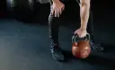 Mężczyzna w czarnych legginsach i butach sportowych podnosi kettlebell 32 kg. Zastanawia się, czy po masażu można iść na trening.