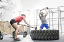 Kobieta i mężczyzna ćwiczą z młotami na oponie w siłowni CrossFit.