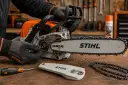 Ręce w rękawiczkach Stihl regulują naciąg łańcucha piły elektrycznej. Obok leży śrubokręt i osłona prowadnicy.