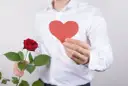Mężczyzna w białej koszuli trzyma czerwoną różę i serce. Idealne bukiety na walentynki.