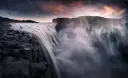 Samotna postać na skalnym brzegu podziwia potężny wodospad. To najpiękniejsze miejsce na ziemi, gdzie natura ukazuje swoją surową siłę.