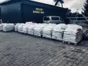 Duże worki z materiałem budowlanym (asfaltem) na paletach przed budynkiem sklepu drogowego.