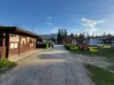 Słoneczny dzień na **camping Oravice**. Drewniany budynek recepcji, przyczepy kempingowe i zielone wzgórza w tle.
