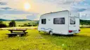 Przyczepa Caravelair zaparkowana na łące o zachodzie słońca. W tle malownicze wzgórza i pola.