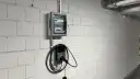 Nowoczesne gniazdo do ładowania samochodu elektrycznego Autel zamontowane na białej, ceglanej ścianie obok skrzynki z bezpiecznikami.
