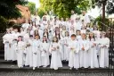 Dzieci w białych strojach komunijnych, z wiankami na głowach, pozują do zdjęcia. Zastanawiasz się, ile kosztuje fotograf na komunię?