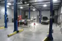 Jasne, jasne oświetlenie w warsztacie samochodowym to podstawa. Widać tu podnośniki, narzędzia i samochody gotowe do naprawy.