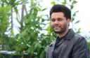 The Weeknd trägt eine schwarze Lederjacke vor einem grünen, unscharfen Hintergrund.