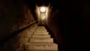 Escaleras de hormigón que bajan hacia una puerta en un sótano oscuro con una luz tenue.