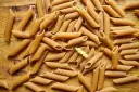 Mnóstwo makaronu pszennego pełnoziarnistego penne i jeden skręcony makaron na drewnianym tle.