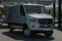 Srebrny bus Mercedes-Benz Sprinter, idealny jako jaki bus na budowę, stoi na parkingu przed nowoczesnym budynkiem.
