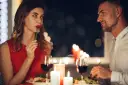 Romantyczna kolacja przy świecach. Ona, w czerwonej sukience, zmysłowo je, a on patrzy na nią z uwielbieniem. Widać oznaki flirtu dziewczyny w jej spojrzeniu.