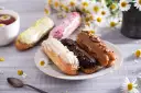 Eklery z czekoladą i profiteroles, ozdobione kwiatami, kuszą smakiem. Idealne na popołudniową herbatę.
